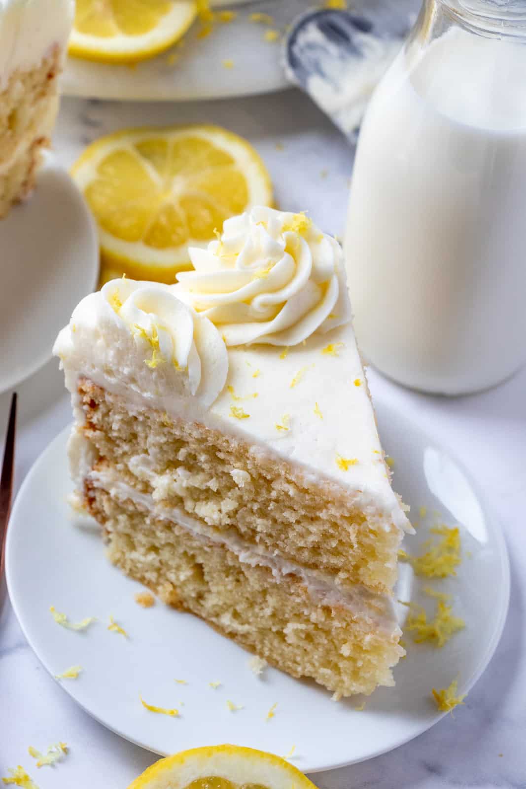 Slice of lemon cake on white plate overhead photo showing top with lemons and milk in background