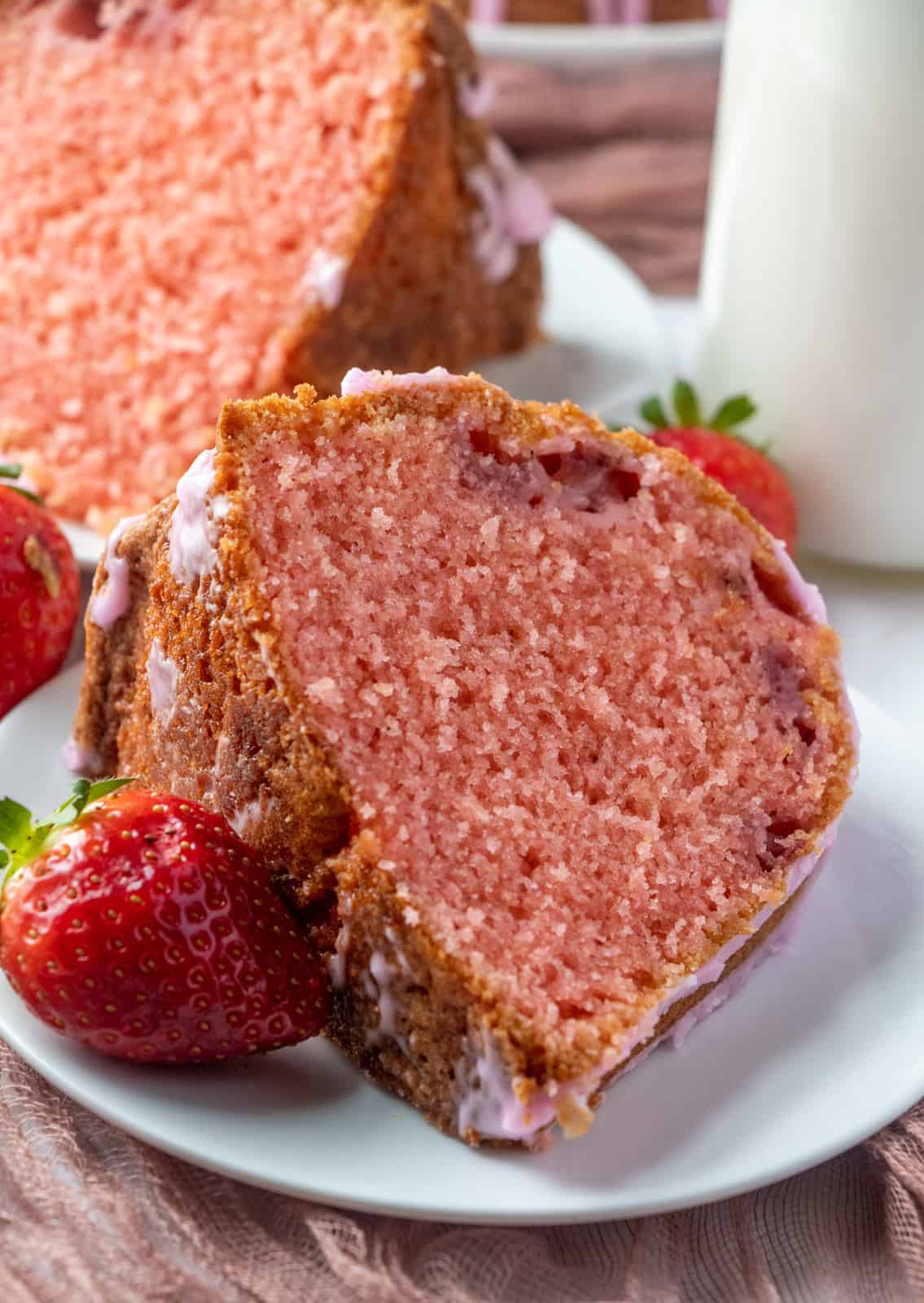 Close up of sliced piece of cake on white plate with strawberry garnish on plate