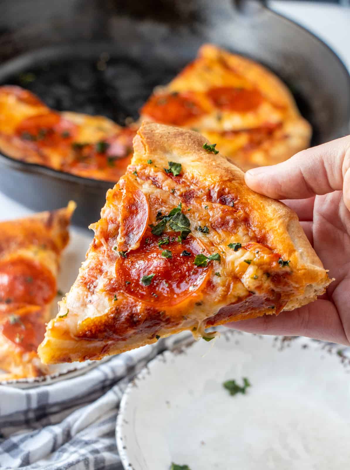 Hand holding slice of pizza topped with basil