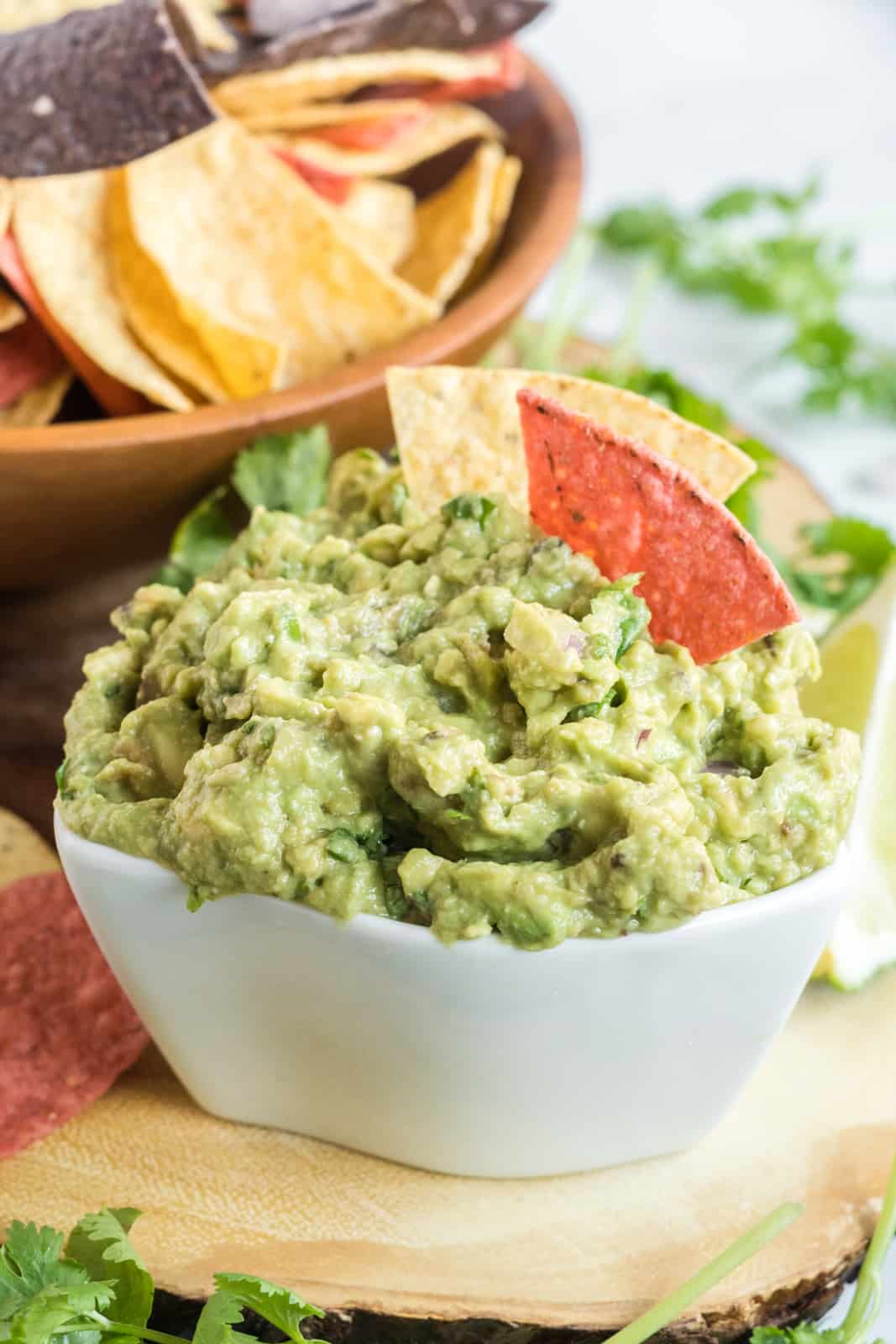 Guacamole in bowl with chips sticking out of it and bowl of chips in background