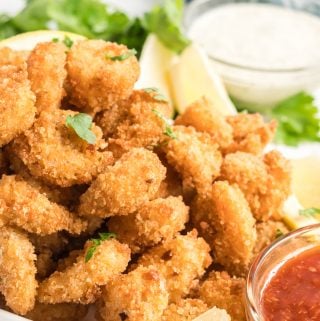 Up close photo of fried shrimp on plate with lemons and sauce