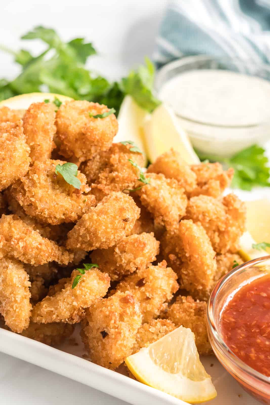 Up close photo of fried shrimp on plate with lemons and sauce