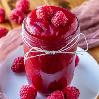 Raspberry sauce in jar topped with raspberries on white plate