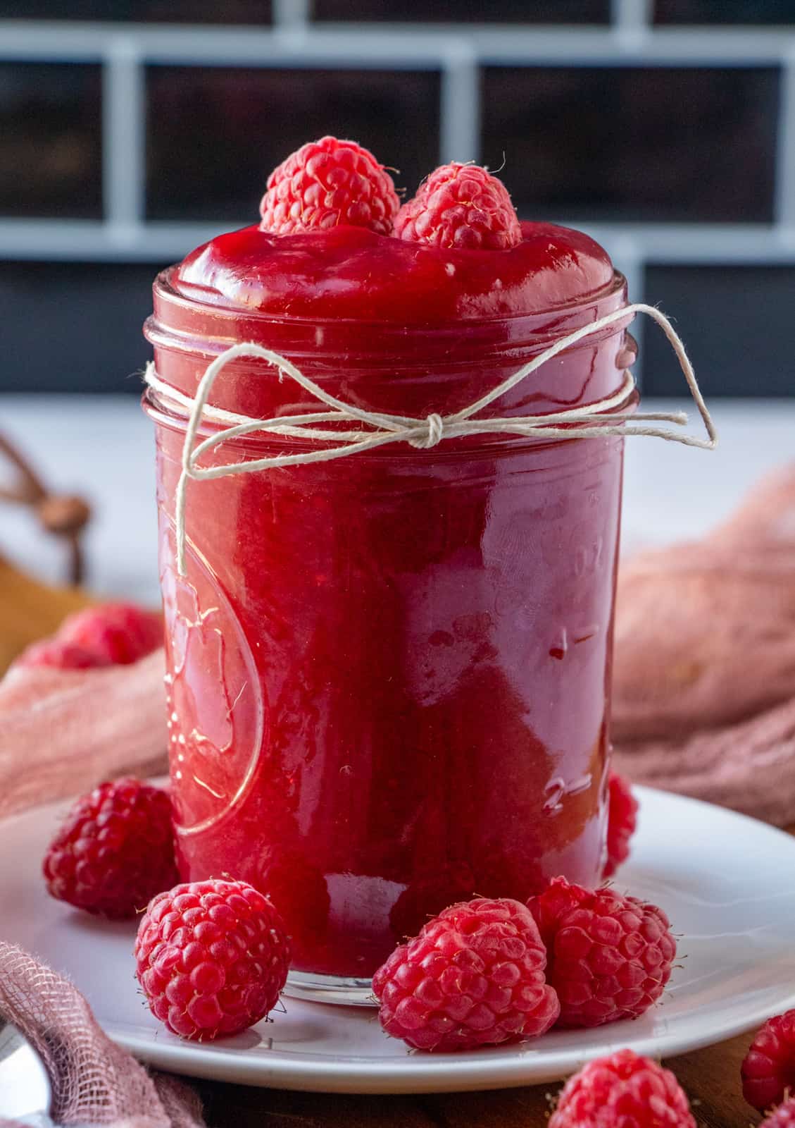white plate with jar full of sauce surrounded by raspberries