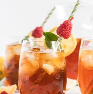 Tea in serving glasses garnished with mint leaves, raspberries and lemon