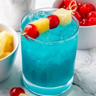Blue Hawaiian Cocktail in glass with ice topped with pineapple and cherries