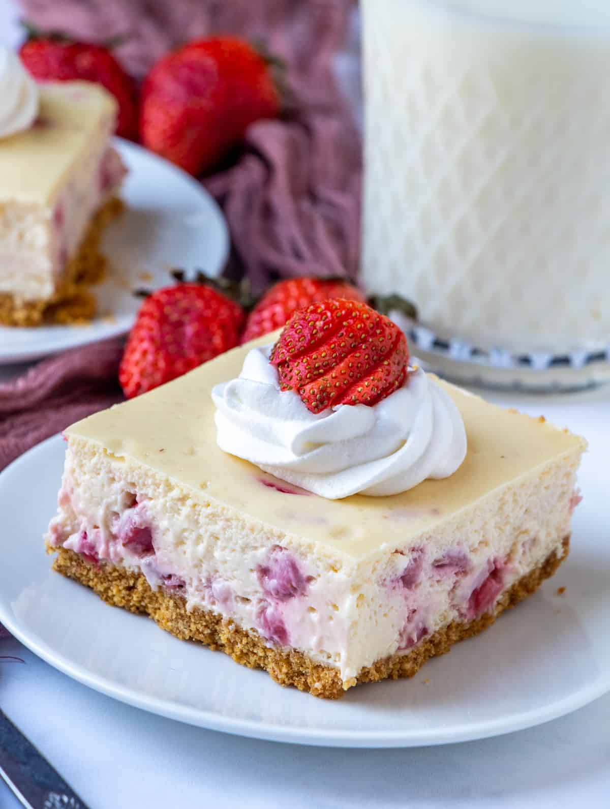 Slice of cheesecake bar on plate with whipped topping and strawberry