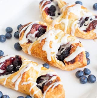 Three danishes on white plate with blueberries