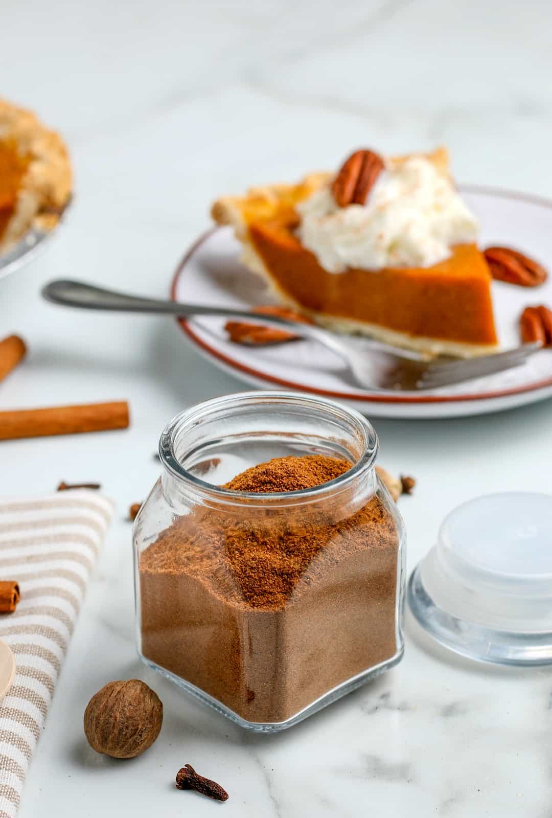 Pumpkin pie spice in glass jar with slice of pumpkin pie in background
