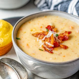 Bowl of soup with bacon and cheese on platter with two spoons