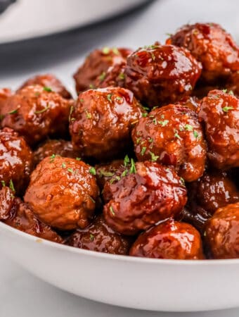 Close up square image of finished meatballs in white bowl.
