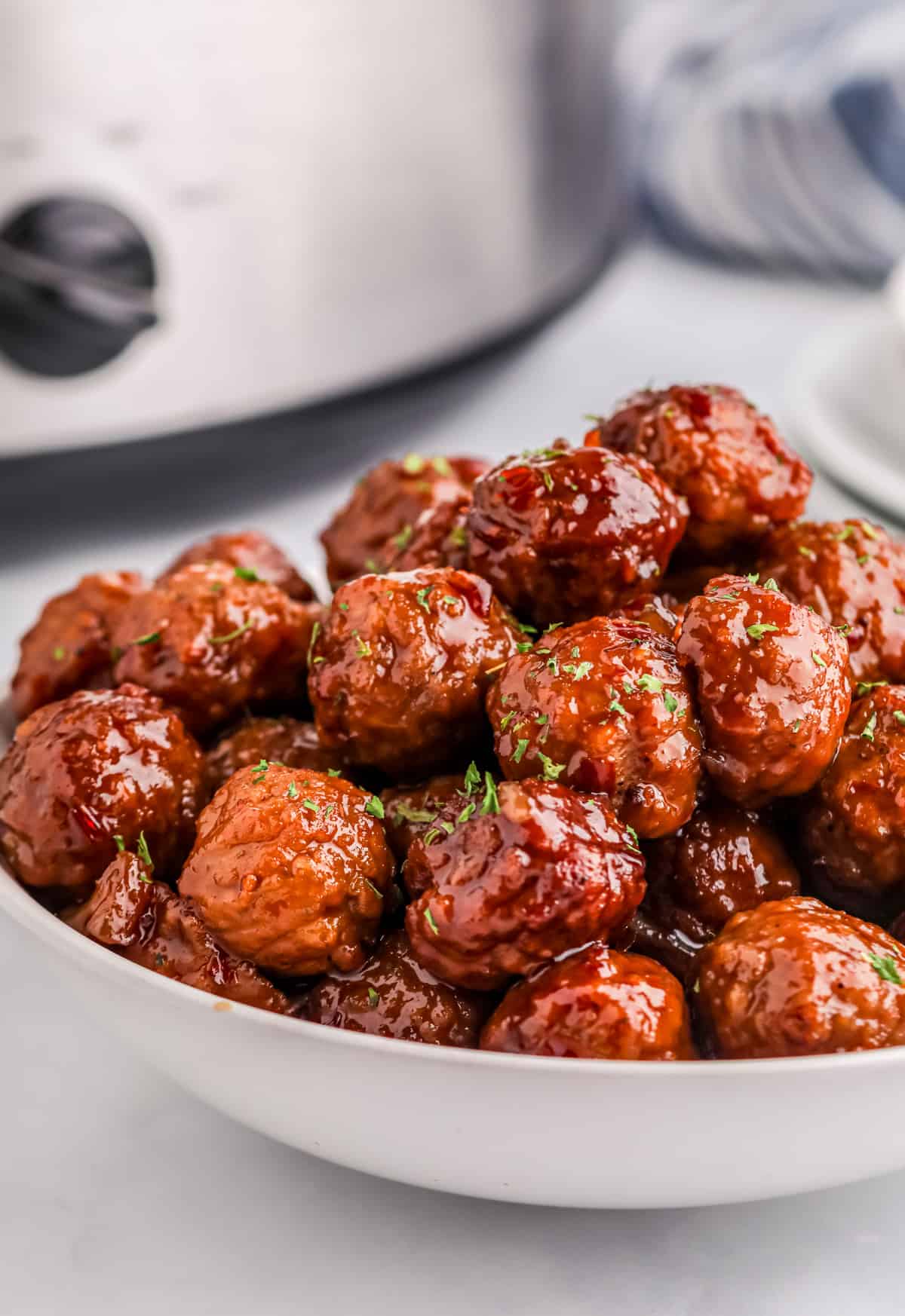 Finished Sweet & Spicy Slow Cooker Meatballs in white bowl in front of slow cooker.