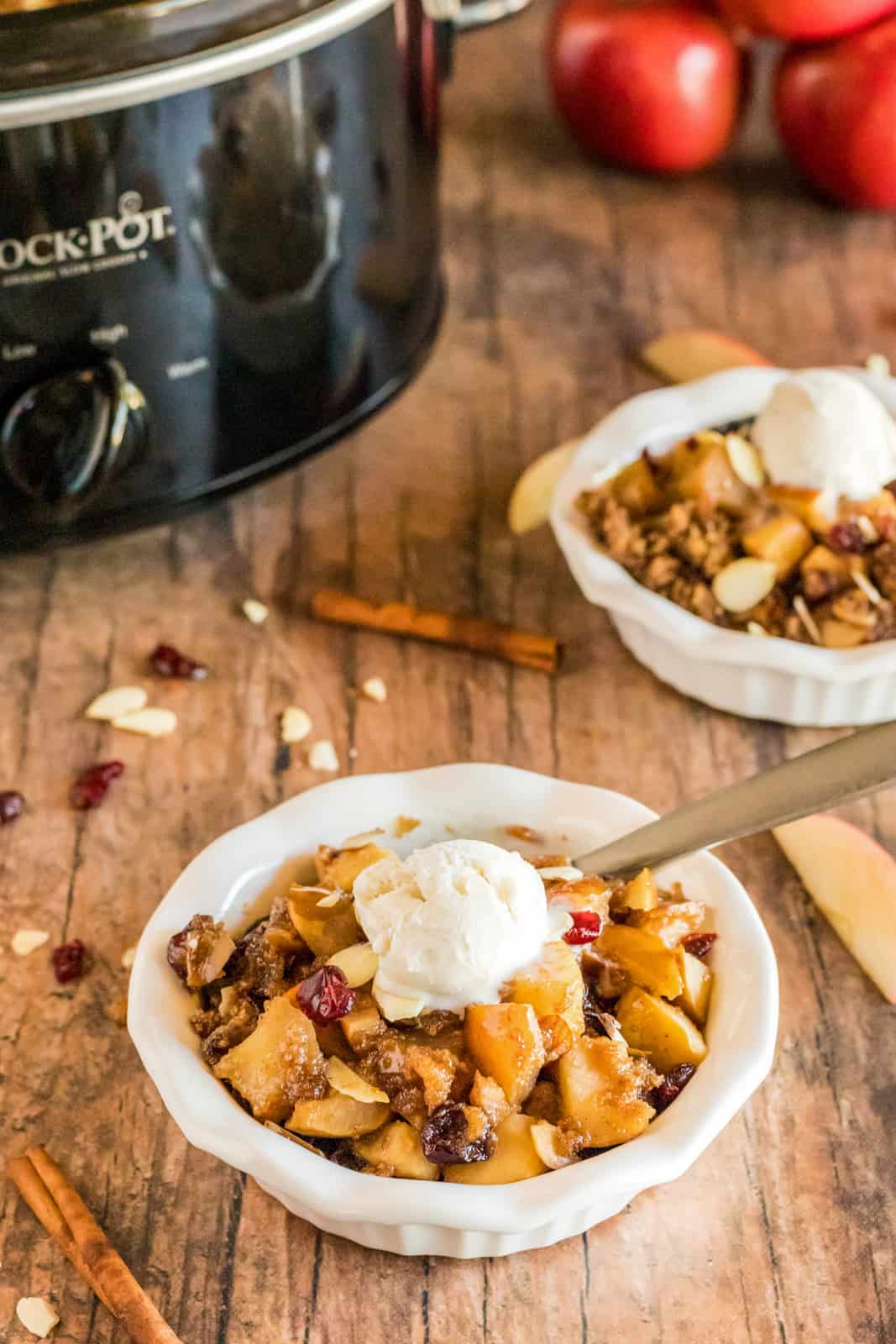 Two bowls of crumble with ice cream and spoon next to crockpot