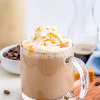 Latte in clear mug topped with whipped cream and caramel drizzle