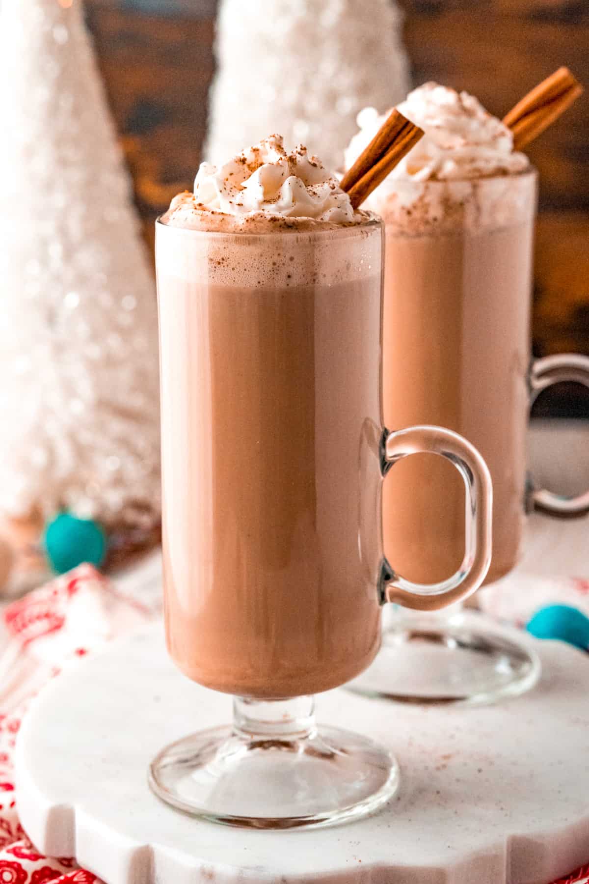 Close up of Eggnog Hot Chocolate in mug topped with whipped cream, garnish and cinnamon stick.