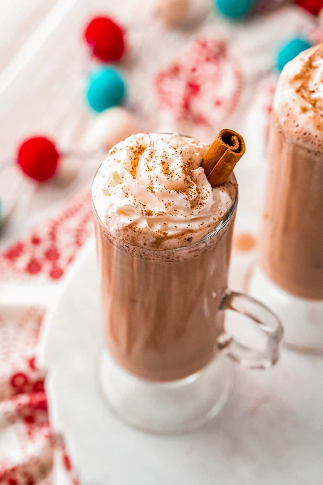 Close up overhead of glass of Eggnog Hot Chocolate topped with whipped cream, nutmeg and cinnamon stick
