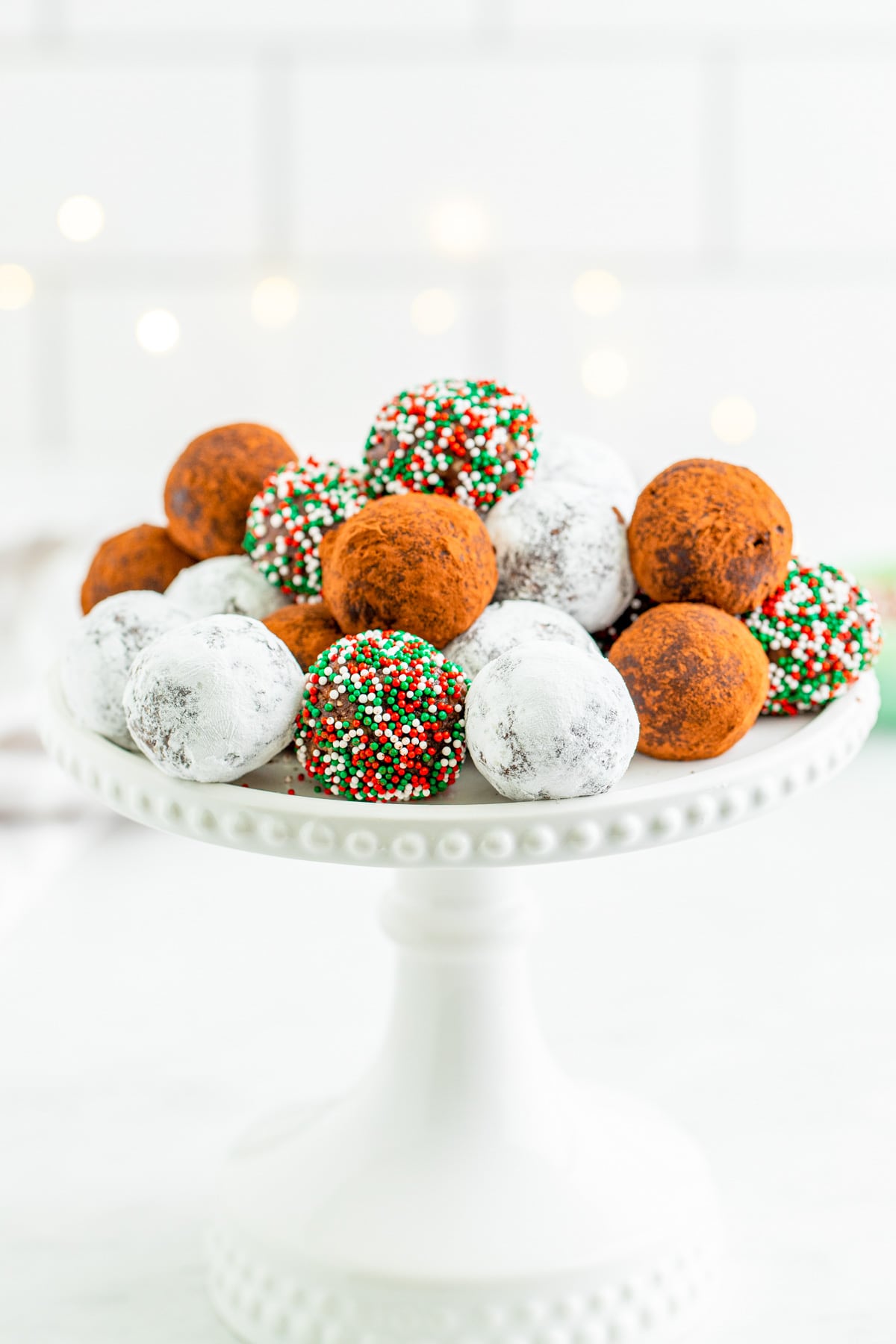 Finished Rum Balls on a white cake stand all rolled in different ingredients.