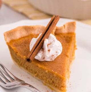 Slice of Sweet Potato Pie on white plate with whipped cream and cinnamon stick