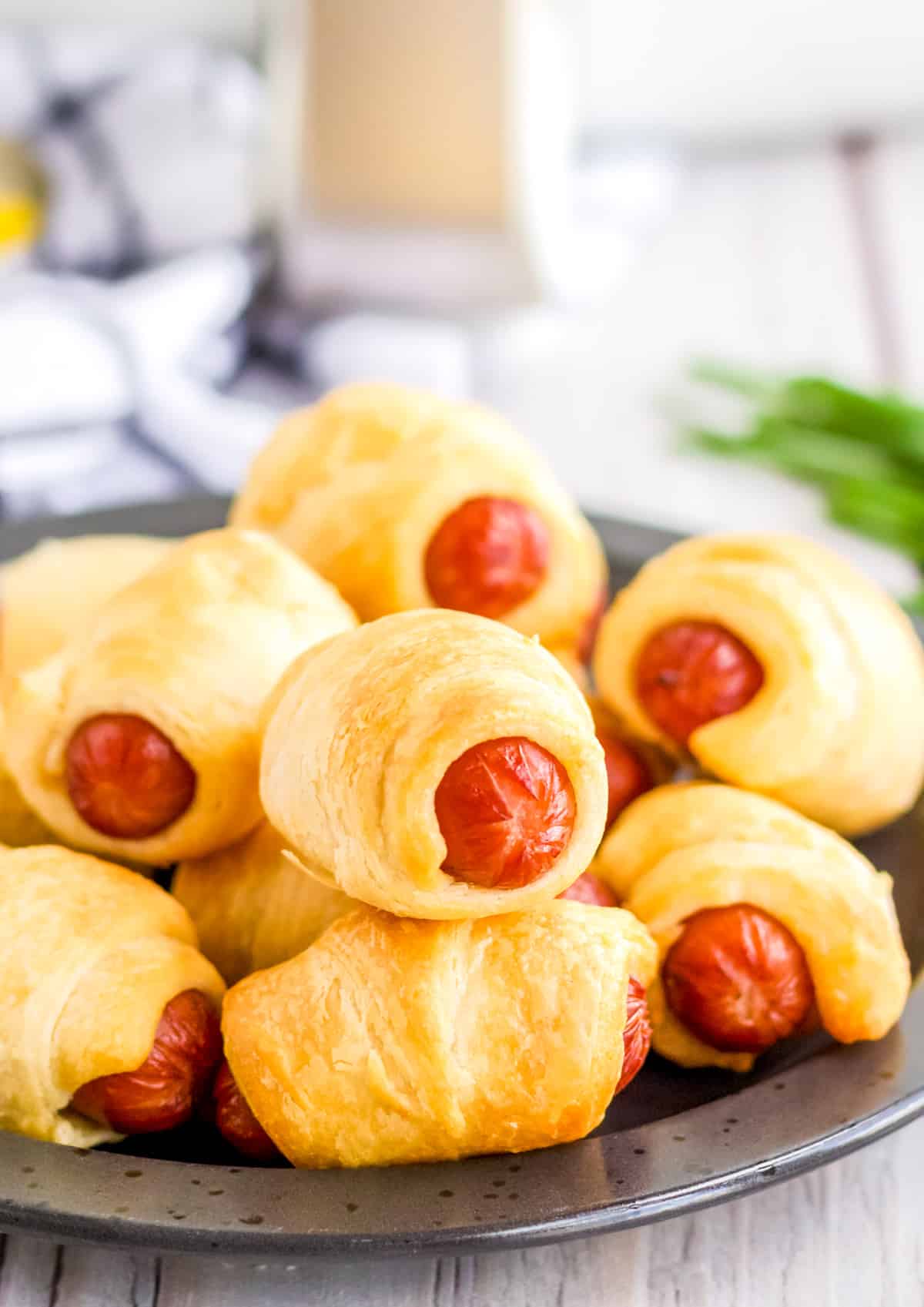 Finished Air Fryer Pigs in a Blanket stacked on a black plate with air fryer in background.