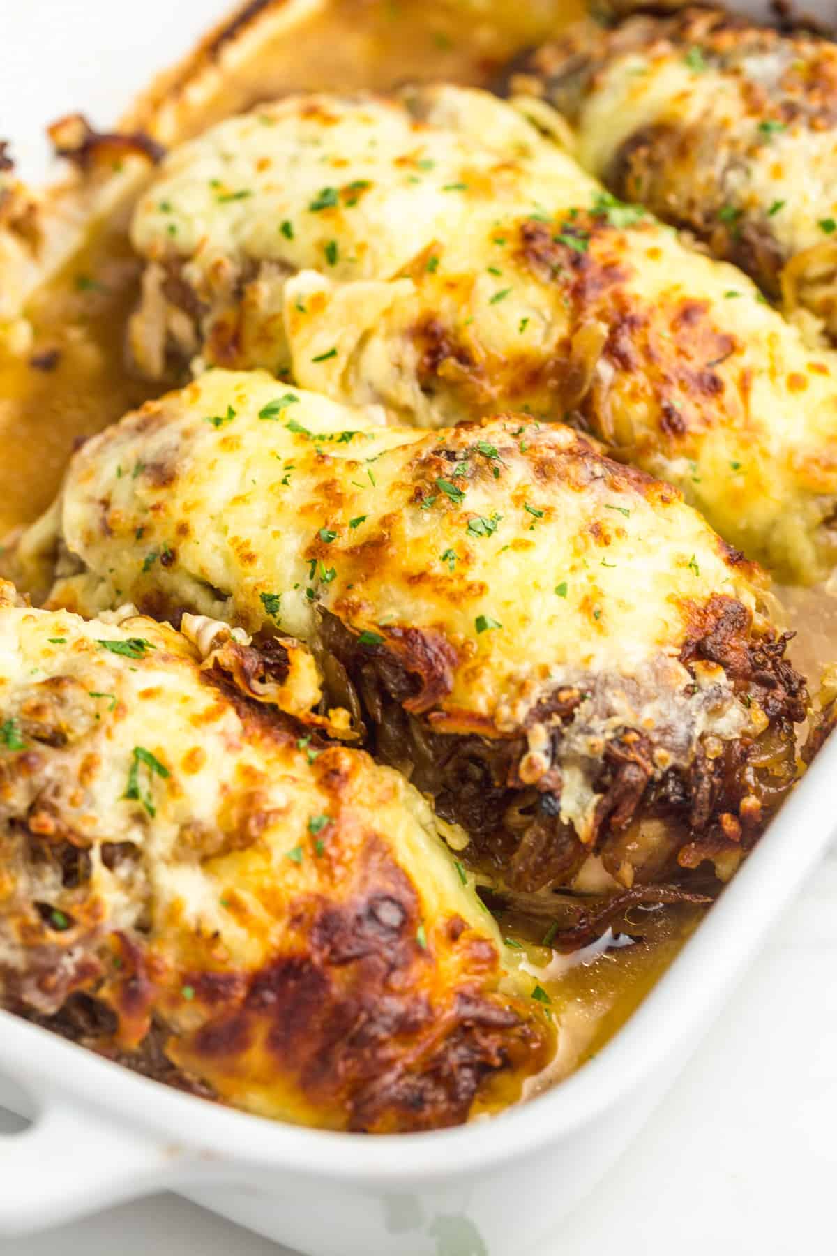 French Onion Chicken in in white baking dish with melted cheese and parsley.