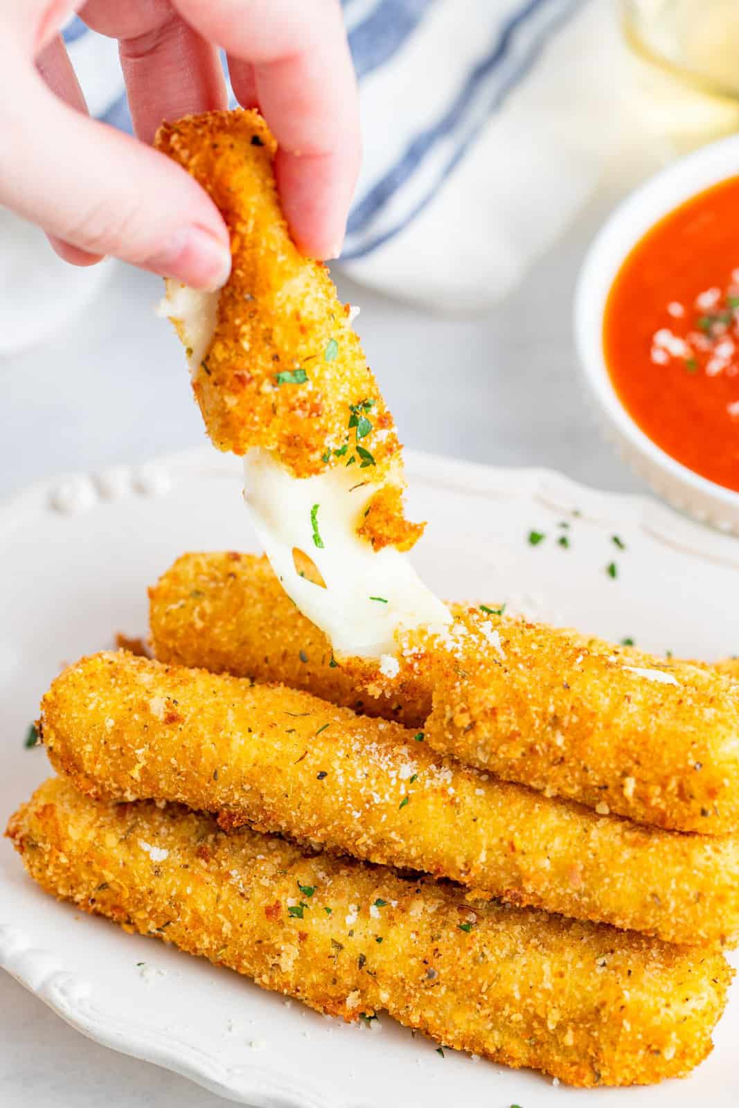 Hand breaking one mozzarella stick apart showing cheese pull