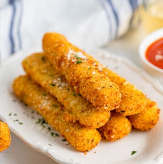 Stacked Mozzarella Sticks on white platter with parsley and parmesan