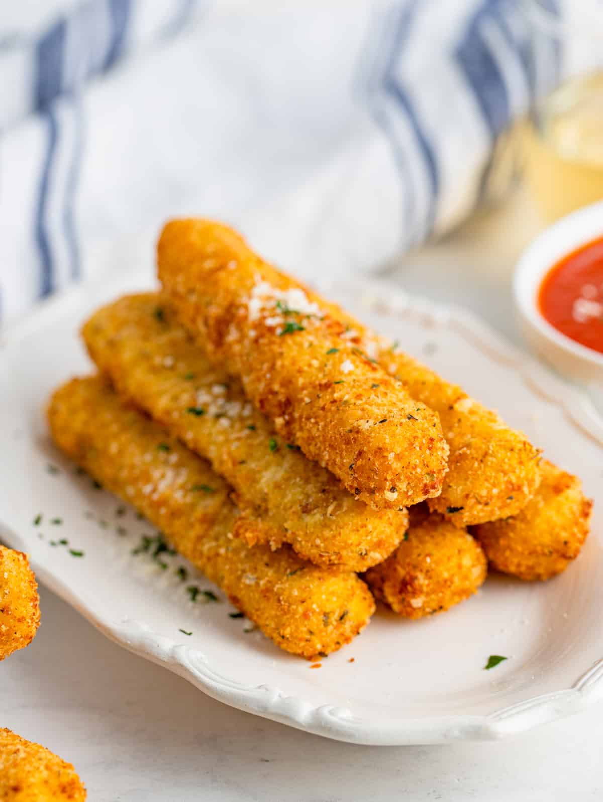Stacked Mozzarella Sticks on white platter with parsley and parmesan