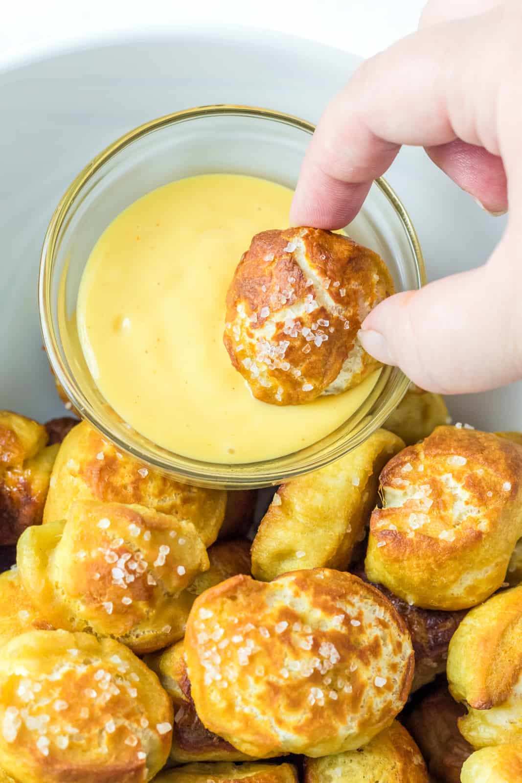 Hand dipping one pretzel bite into cheese sauce