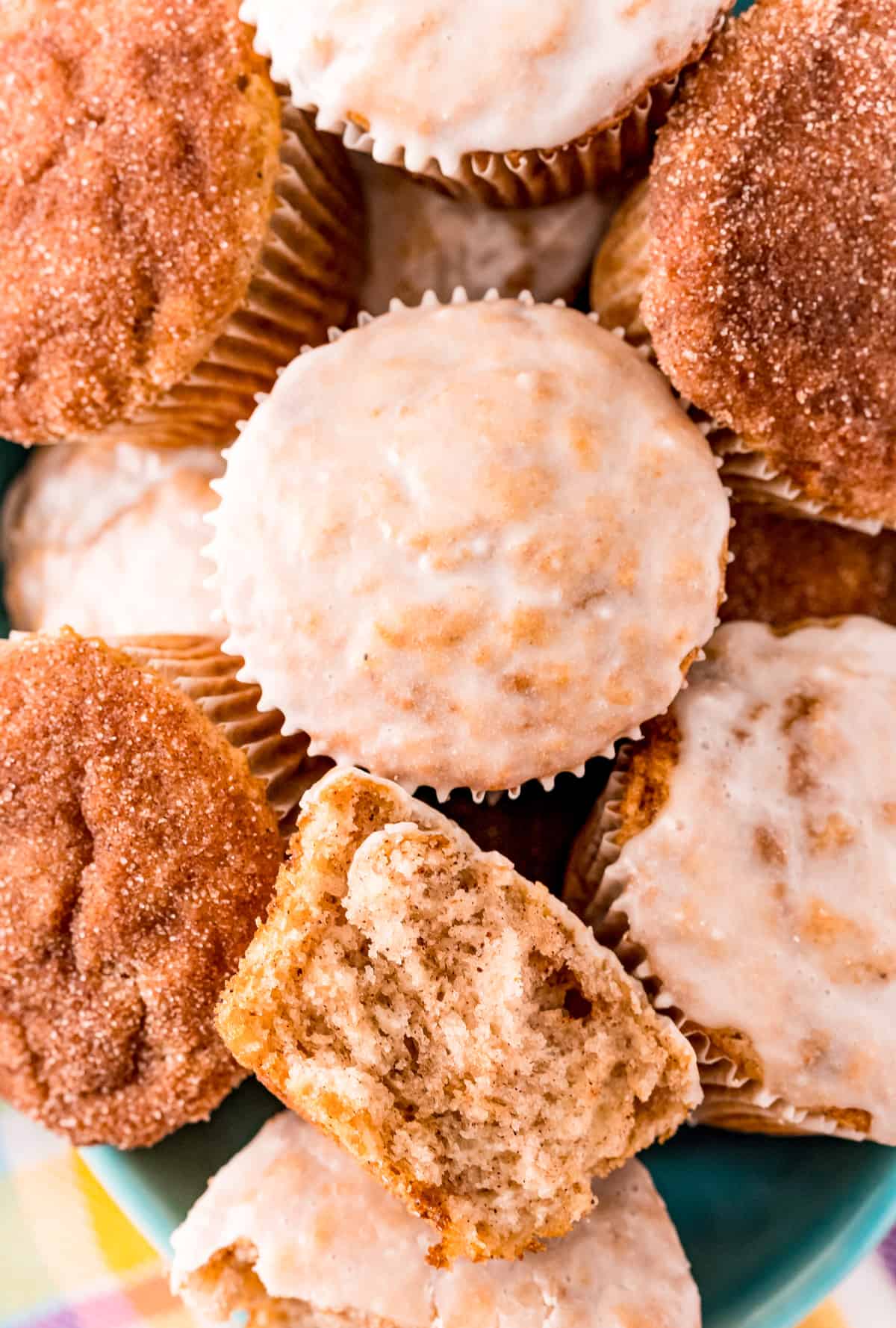 Overhead of stacked Cinnamon Muffins some glazed and some dipped in cinnamon sugar with one split in half.