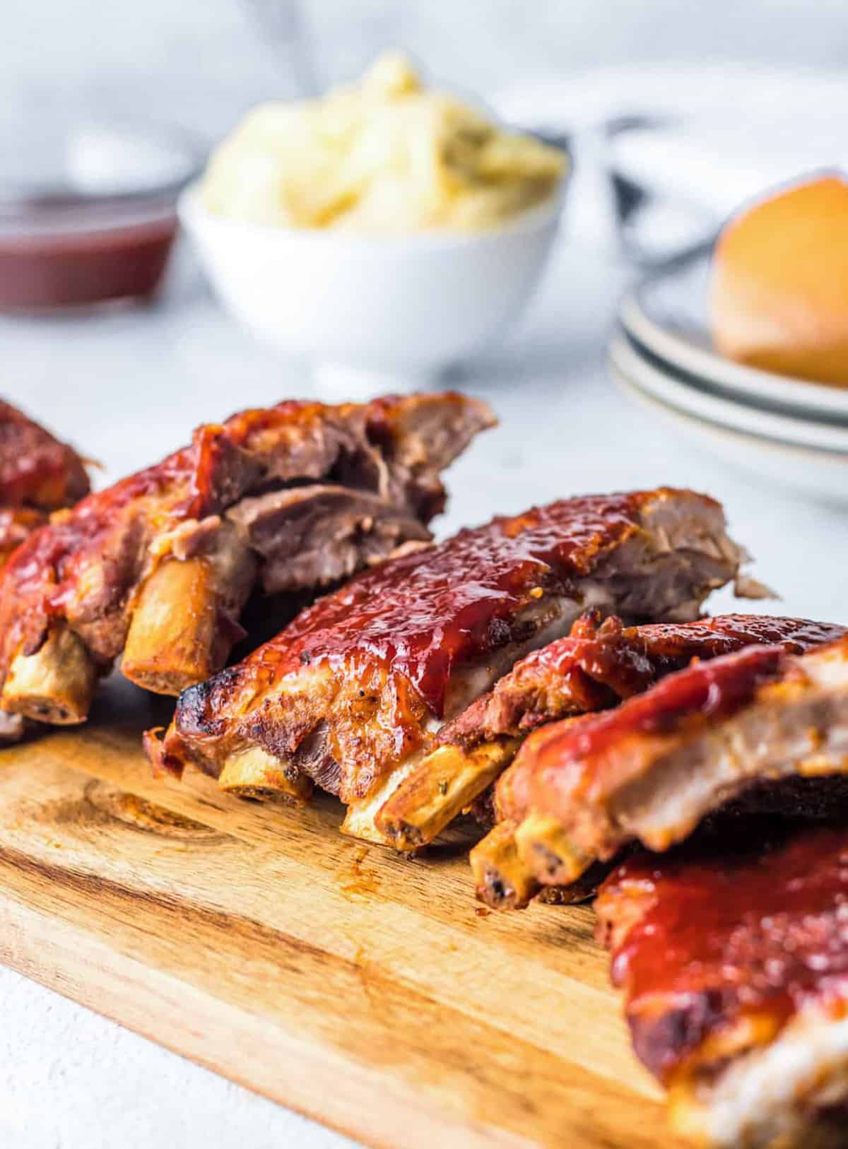 Sliced Instant Pot BBQ Ribs on wooden board with side dishes in background.
