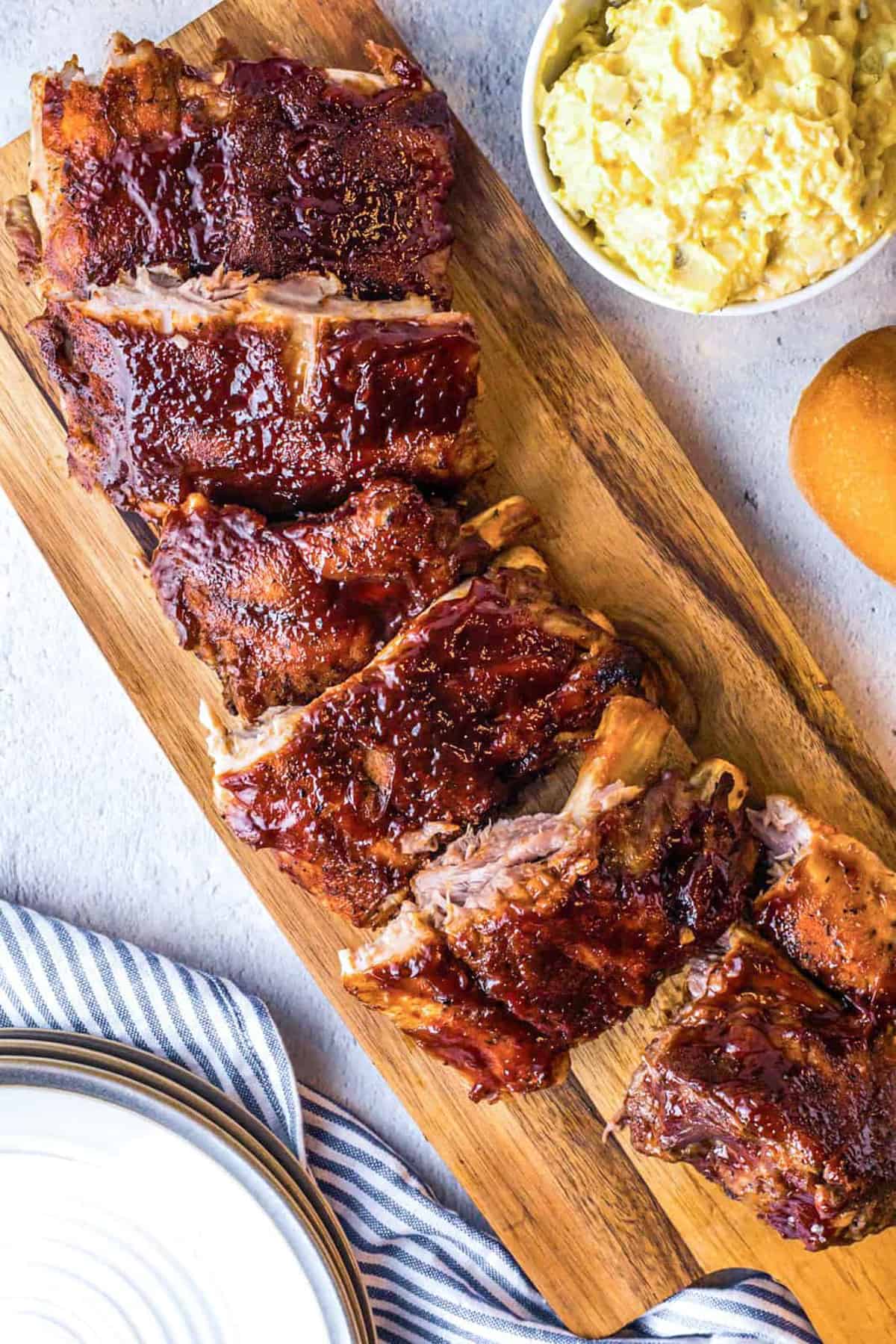 Overhead of Instant Pot BBQ Ribs on wooden board with potato salad in bowl next to them.