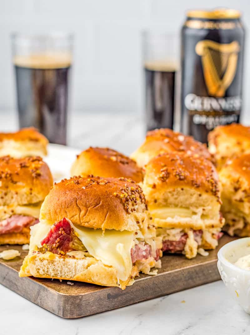 Sliders on wooden platter showing melted cheese with corned beef popping through.