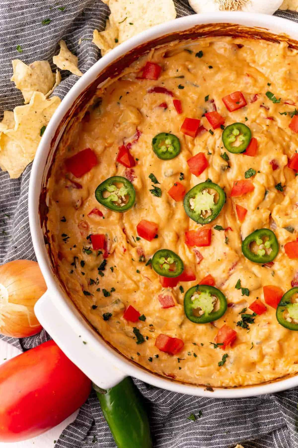 Overhead of Baked Queso Dip in white baking dish topped with tomatoes and jalapenos.
