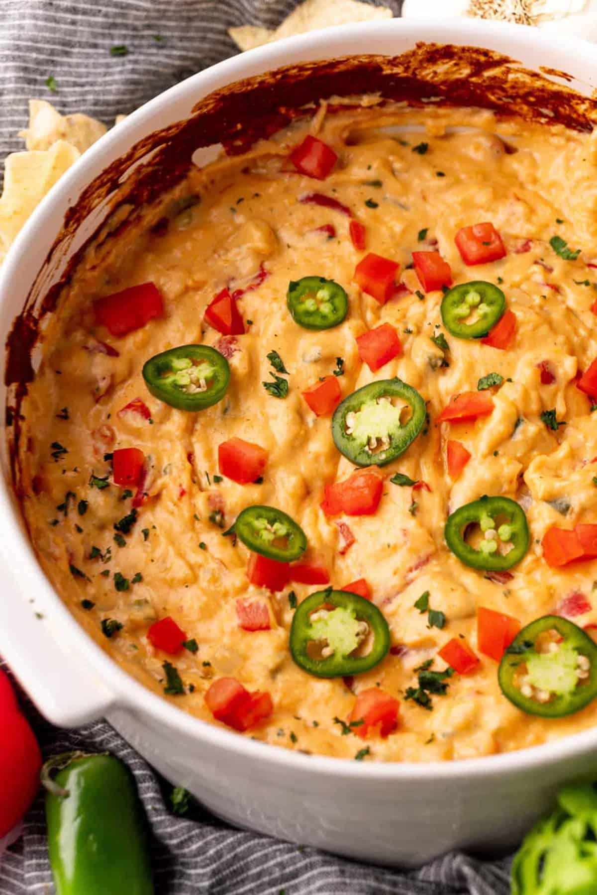 Finished Baked Queso Dip in white baking dish topped with diced tomatoes and sliced jalapenos.