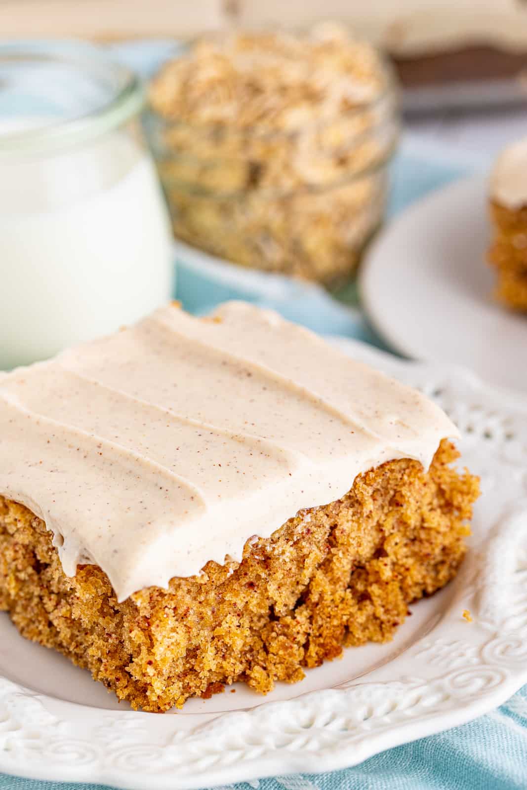 Slice of Old-Fashioned Oatmeal Cake on white plate with milk and oats in background