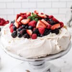 Square photo of Pavlova on cake stand topped with whipped cream and fruit
