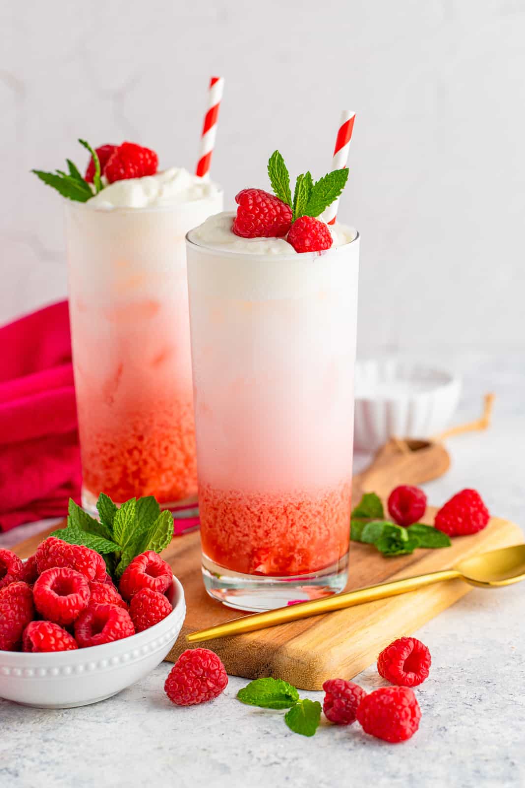 Two Italian Sodas in glass on wooden board surrounded by raspberries and mint