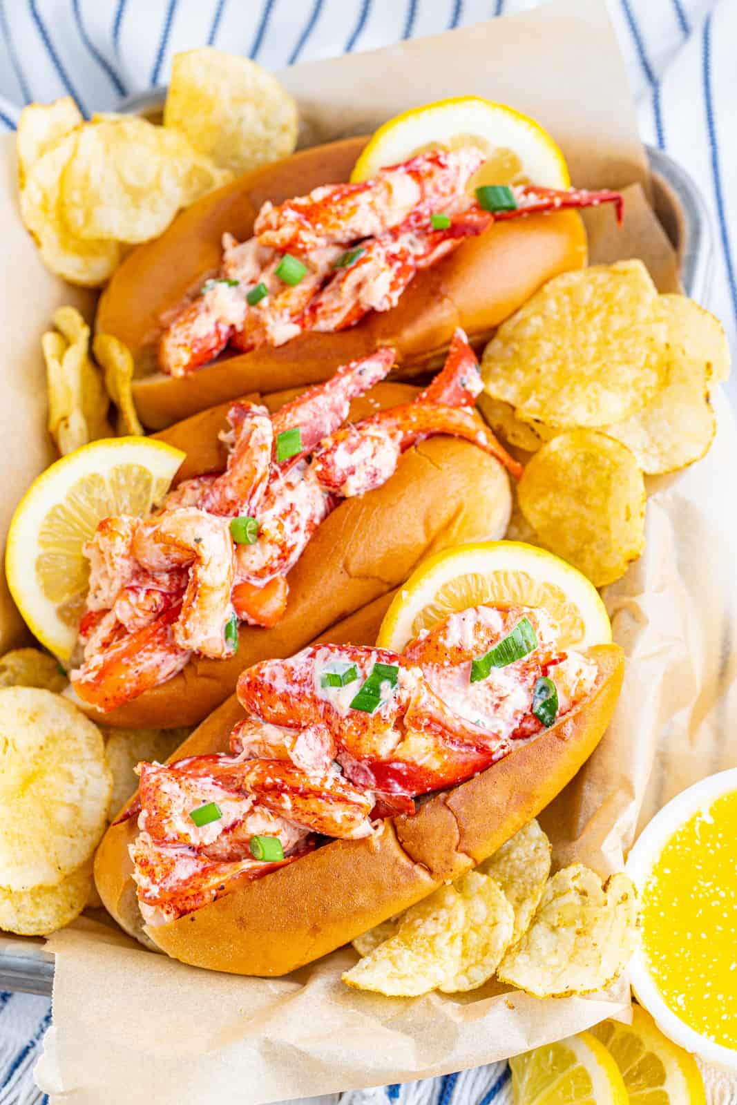 Overhead photo of three Lobster Rolls on parchment Lind tray with chips and lemon