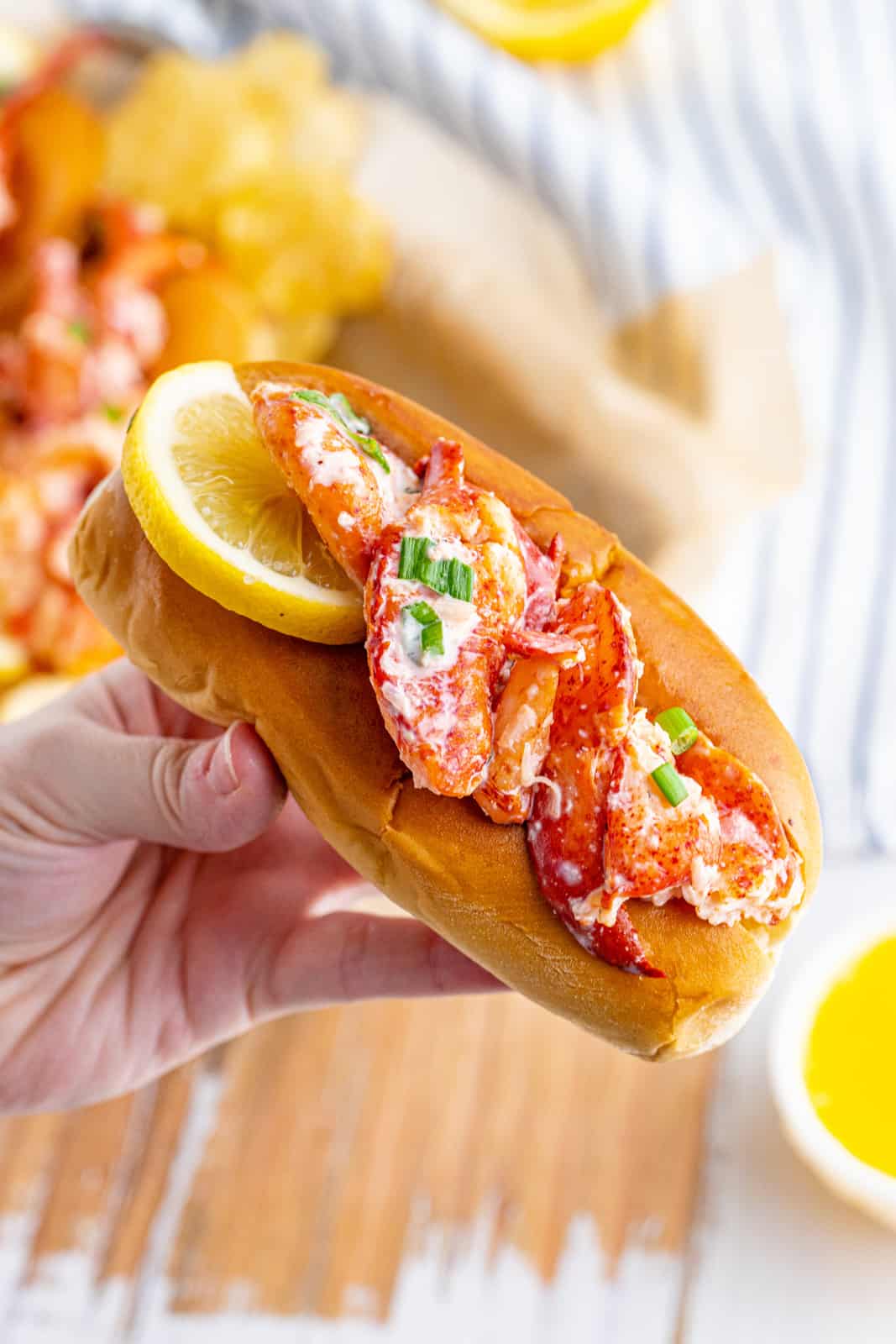 Hand holding up one Lobster roll garnished with lemon slice