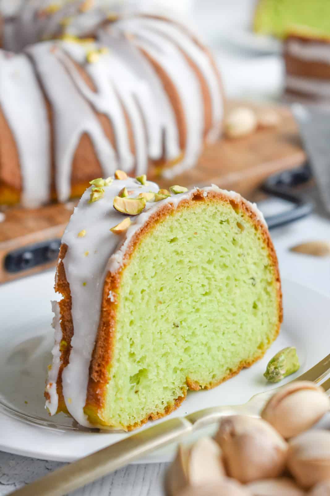 One slice of Pistachio Cake on white plate with cake in background