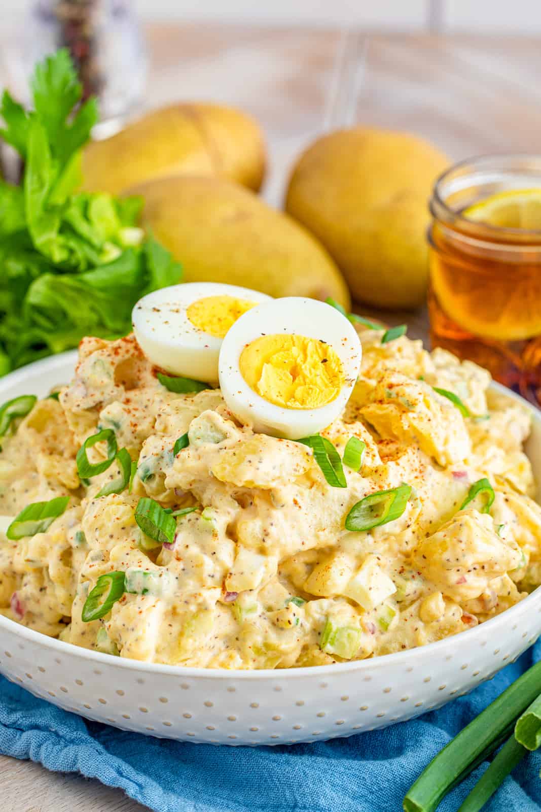 Potato Salad in white bowl topped with green onions and half a hard-boil egg