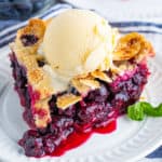 Square image of slice of The Best Blueberry Pie Recipe on white plate with ice cream