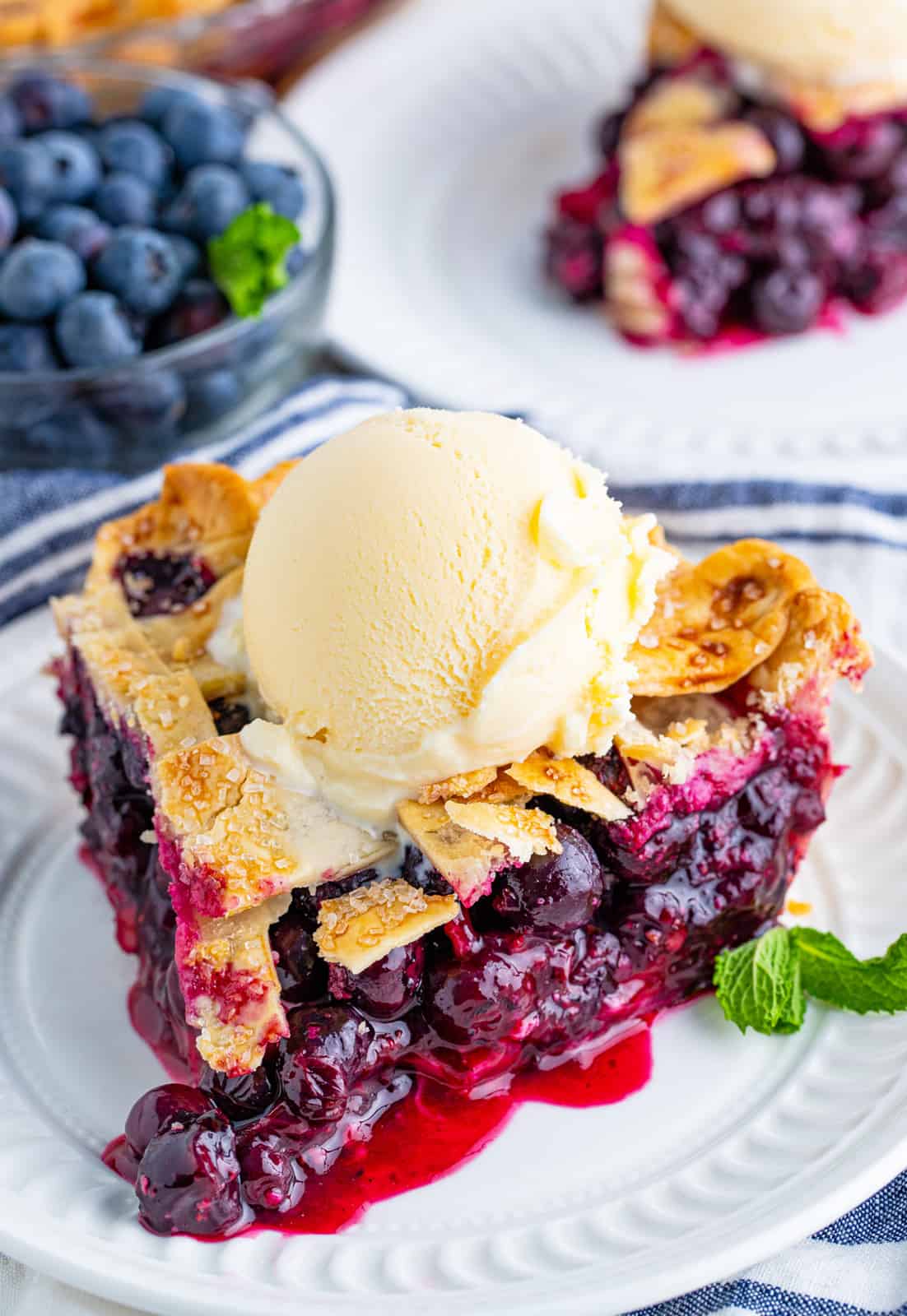 Slice of Blueberry Pie on white plate topped with ice cream
