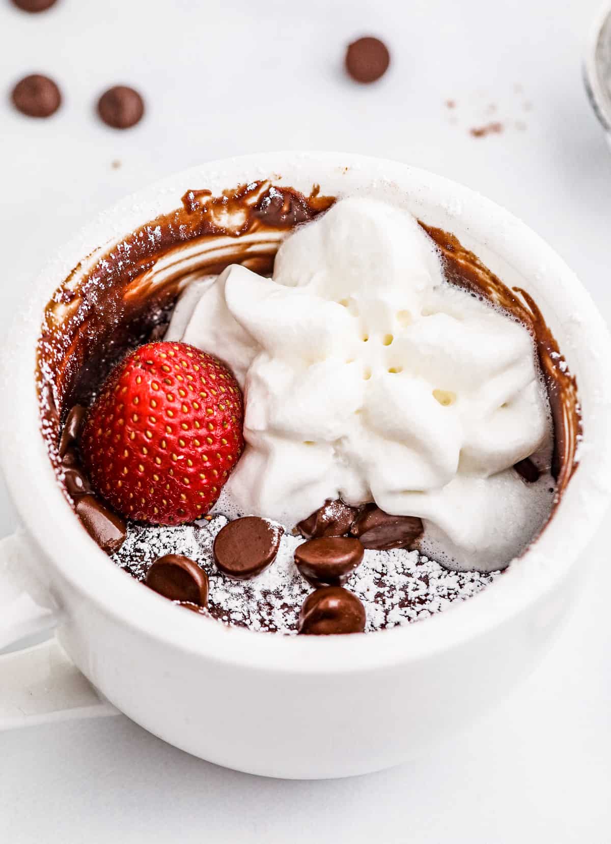 Finished Brownie in a Mug topped with powdered sugar, whipped cream and a strawberry.