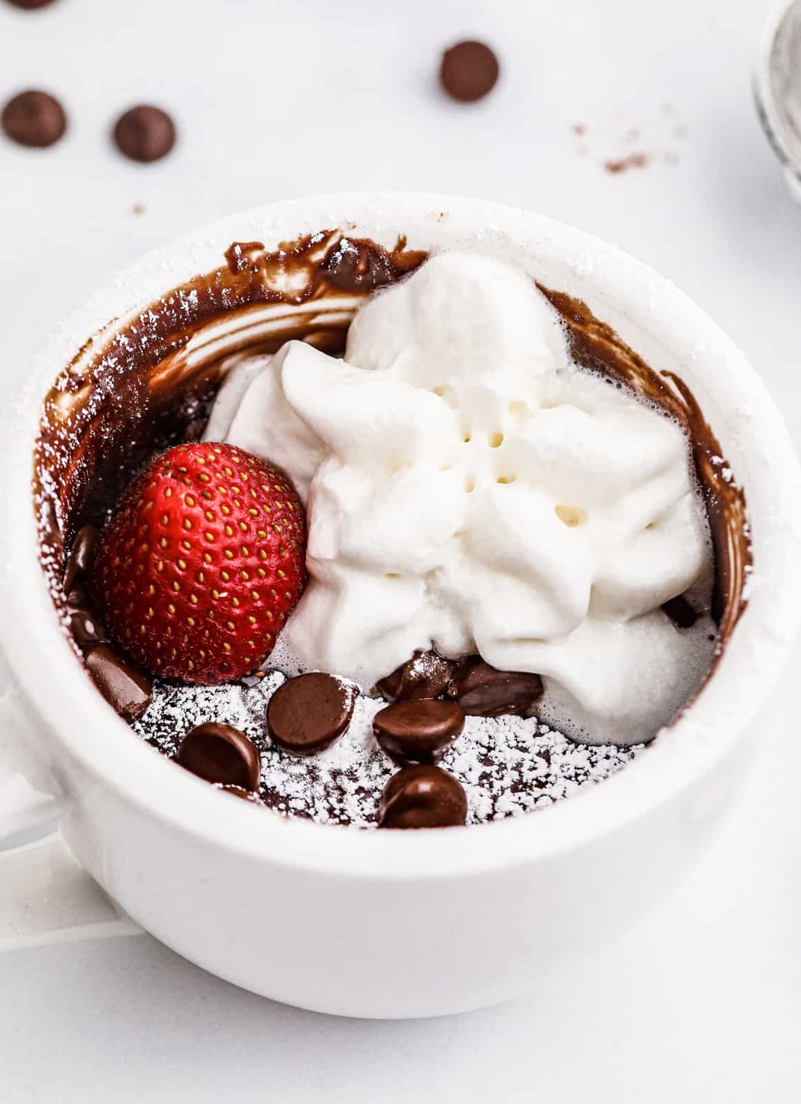 Finished Brownie in a Mug topped with powdered sugar, strawberry and whipped cream