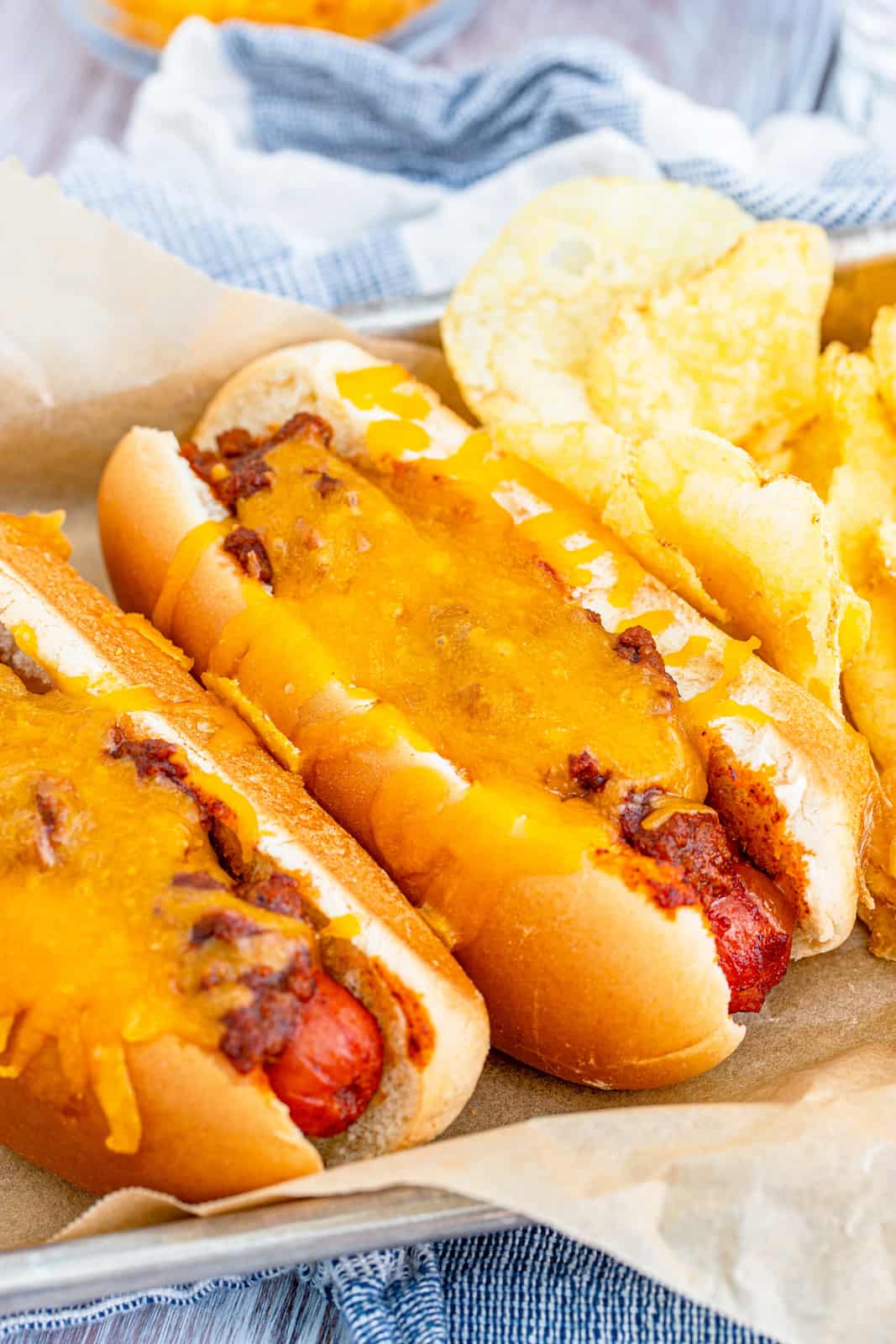 Two Chili Dogs on pan with parchment paper underneath served with chips.