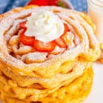 Close up of stacked Funnel Cake Recipe with strawberries, powdered sugar and whipped cream square image
