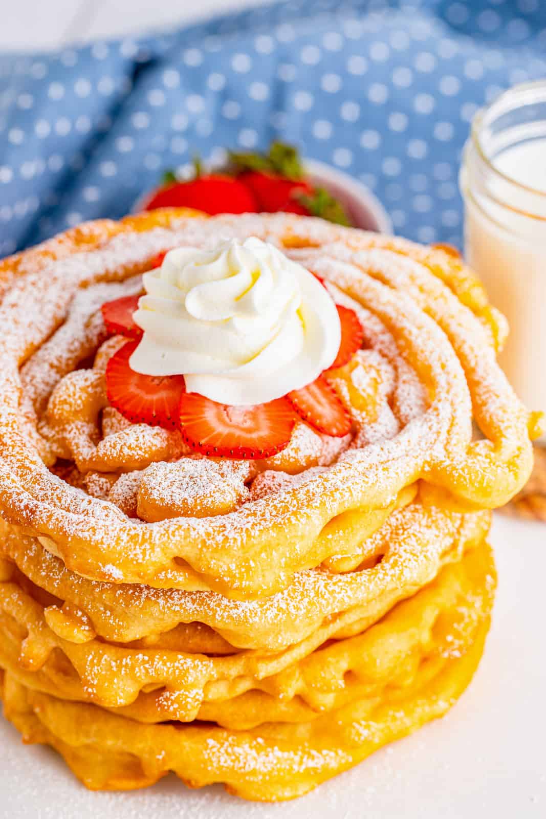 Stacked Funnel Cake Recipe showing top funnel cake topped with Strawberries, powdered sugar and whipped cream