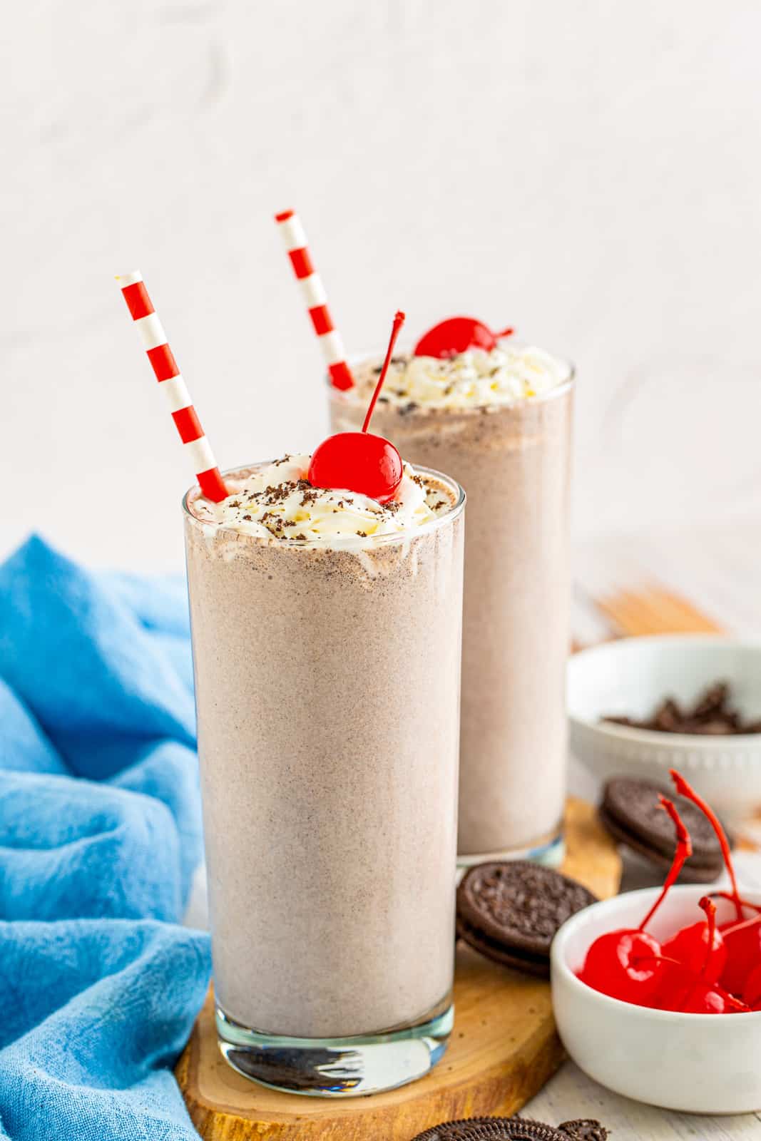 Two milkshakes on wooden board with straws and cherries