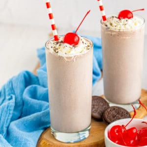 Square image of two milkshakes with whipped cream, cherries and straws